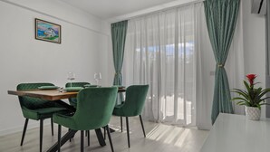 A dining area with a wooden table and green chairs, a potted plant, and a painting on the wall. - The Green Oasis (București)