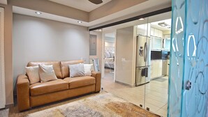 A modern living room with a leather sofa, a glass door leading to a kitchen, and a ceiling fan. - New Listing! Beachfront Luxury at Tortuga – Indoor/Outdoor Pool - 3 BDRM (Siesta Key)