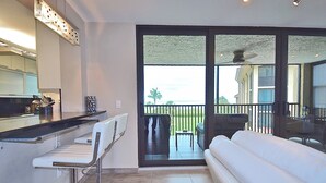 A modern kitchen with a bar area, a white sofa, and a balcony with outdoor furniture. - New Listing! Beachfront Luxury at Tortuga – Indoor/Outdoor Pool - 3 BDRM (Siesta Key)