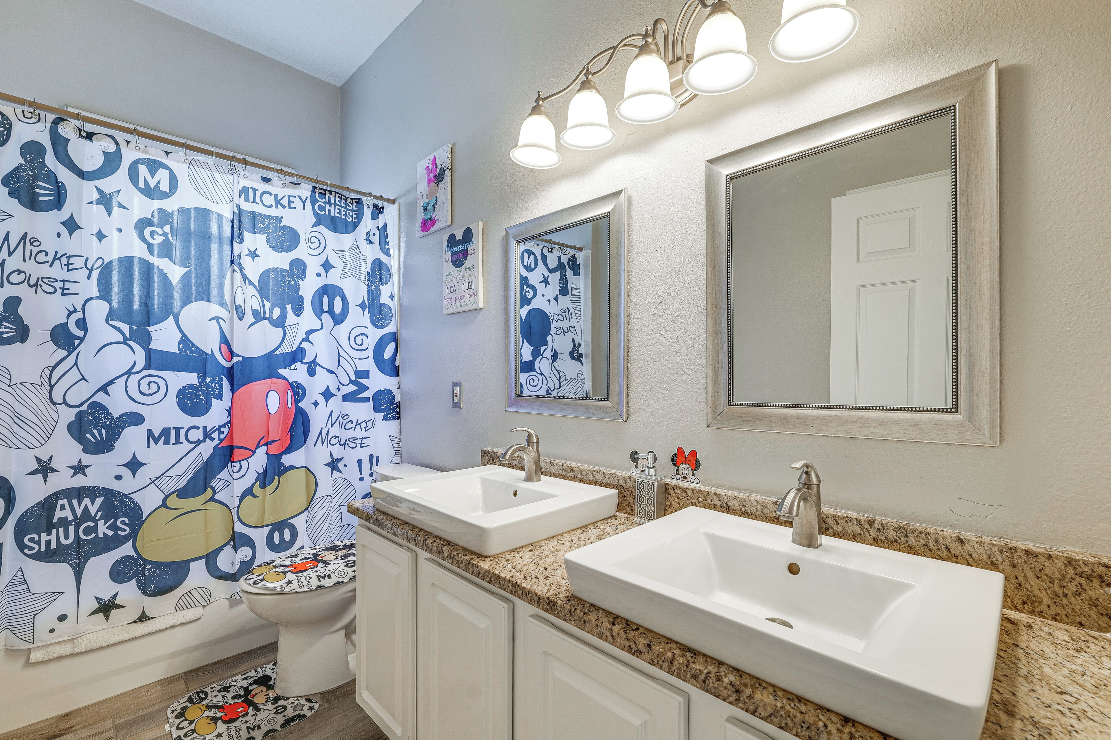 A bathroom with Mickey Mouse-themed shower curtain, two sinks, and a large mirror.
