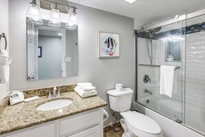 A bathroom with a granite countertop, two sinks, a toilet, a glass-enclosed shower, and a framed fish artwork on the wall. - 3BR Beachfront Condo w/ Pools & Balcony (South Padre Island)