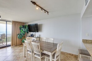 A dining area with a table, chairs, a TV, and a plant. - 3BR Beachfront Condo w/ Pools & Balcony (South Padre Island)