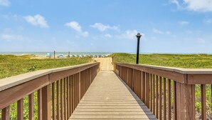 En träpromenad som leder till en strand med strandstolar och parasoller.
