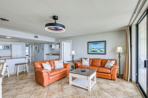 A spacious living area with two orange leather sofas, a coffee table, a ceiling light, a painting, and a view through a large window. - 3BR Beachfront Condo w/ Pools & Balcony (South Padre Island)