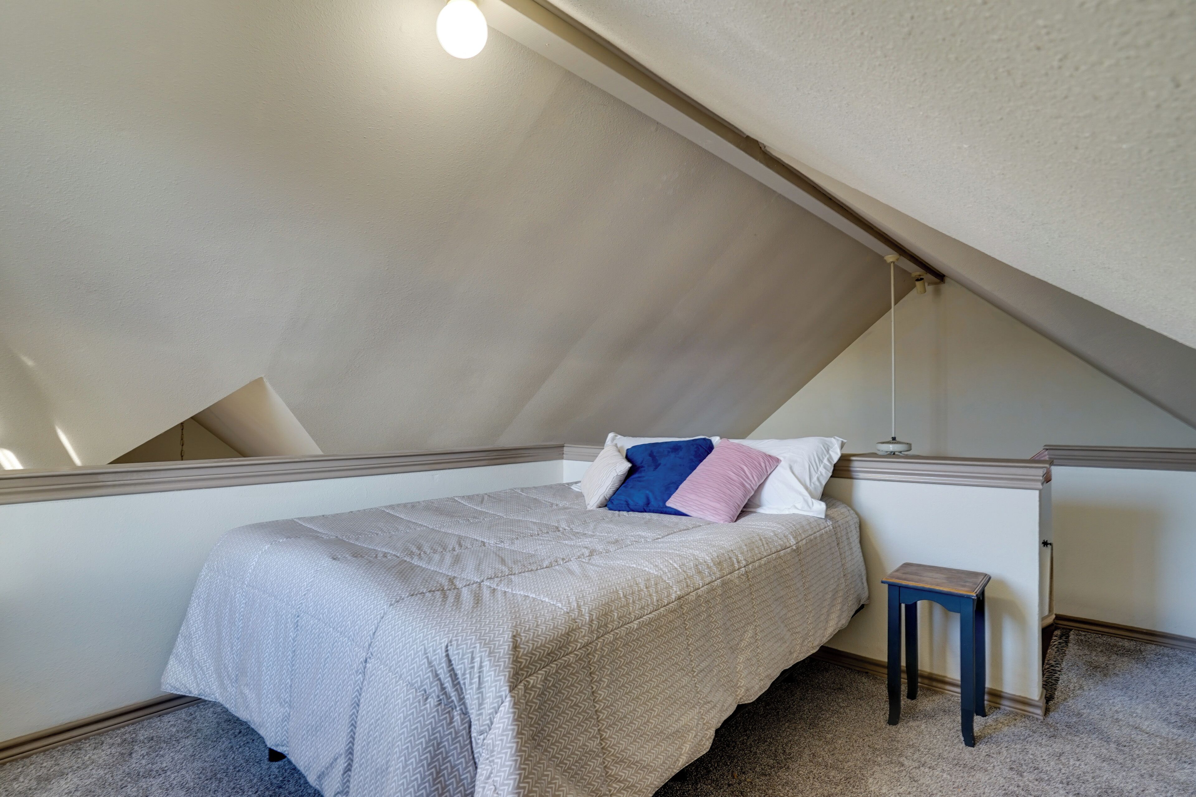 A bedroom with a sloped ceiling, a bed with a patterned bedspread, a bedside table, and a nightstand.