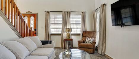 A living room with a sofa, a glass coffee table, a chair, a lamp, and a TV mounted on the wall.