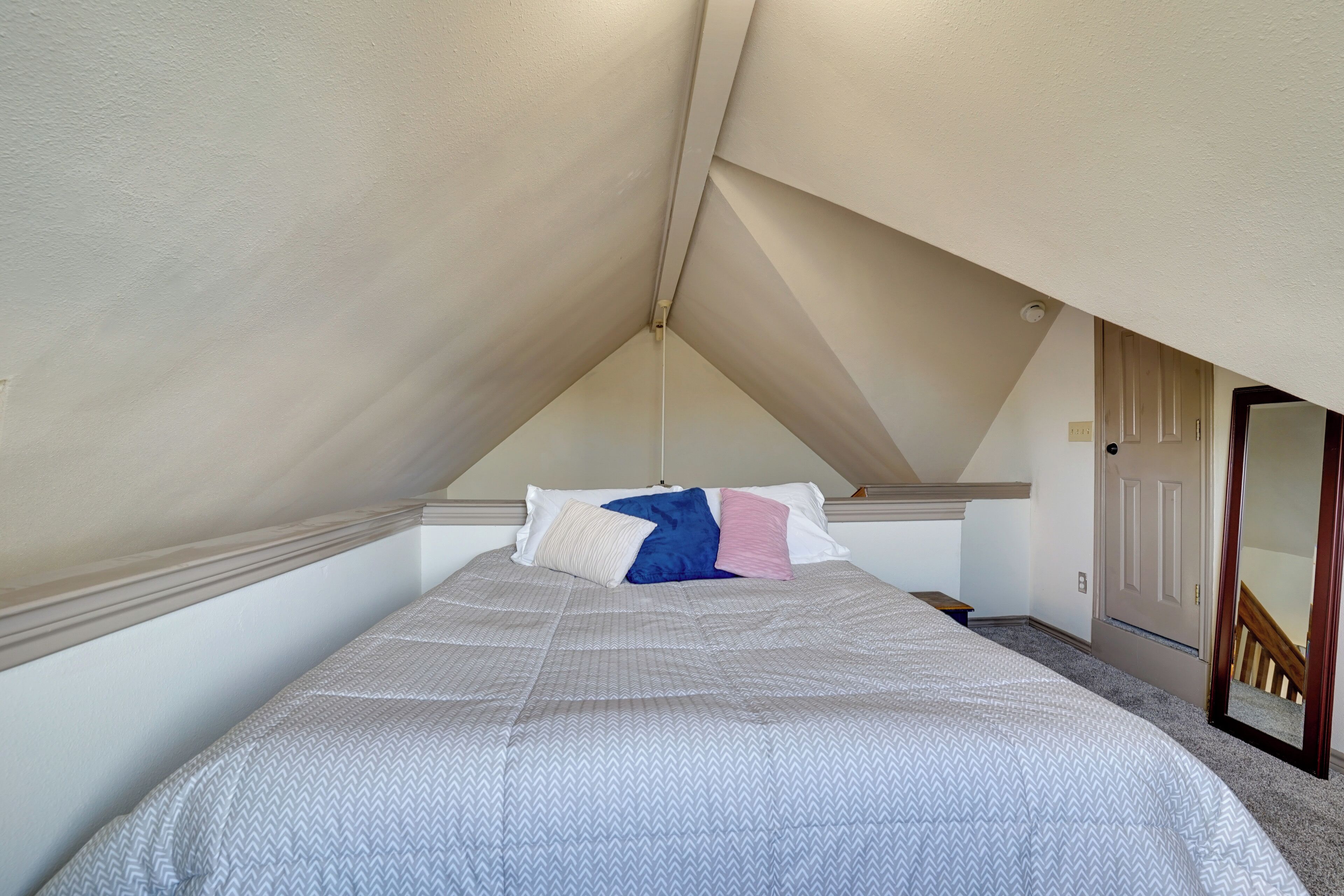 Een slaapkamer met een schuine plafond, een bed met een gestreept sprei, en een deur naar een gang.