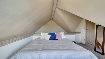 Een slaapkamer met een schuine plafond, een bed met een gestreept sprei, en een deur naar een gang.