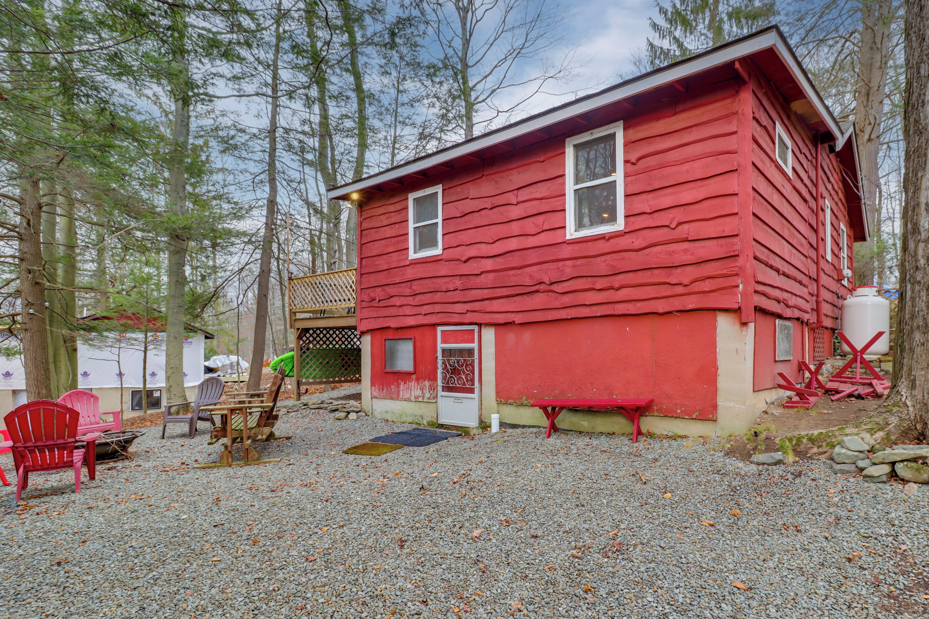 A red cabin with a gravel ground, surrounded by trees.