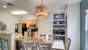 A modern kitchen with wooden cabinets, a dining area with a table and chairs, and a hanging light fixture. - Walk to Beach & Dining: Corpus Christi Townhome (Corpus Christi)