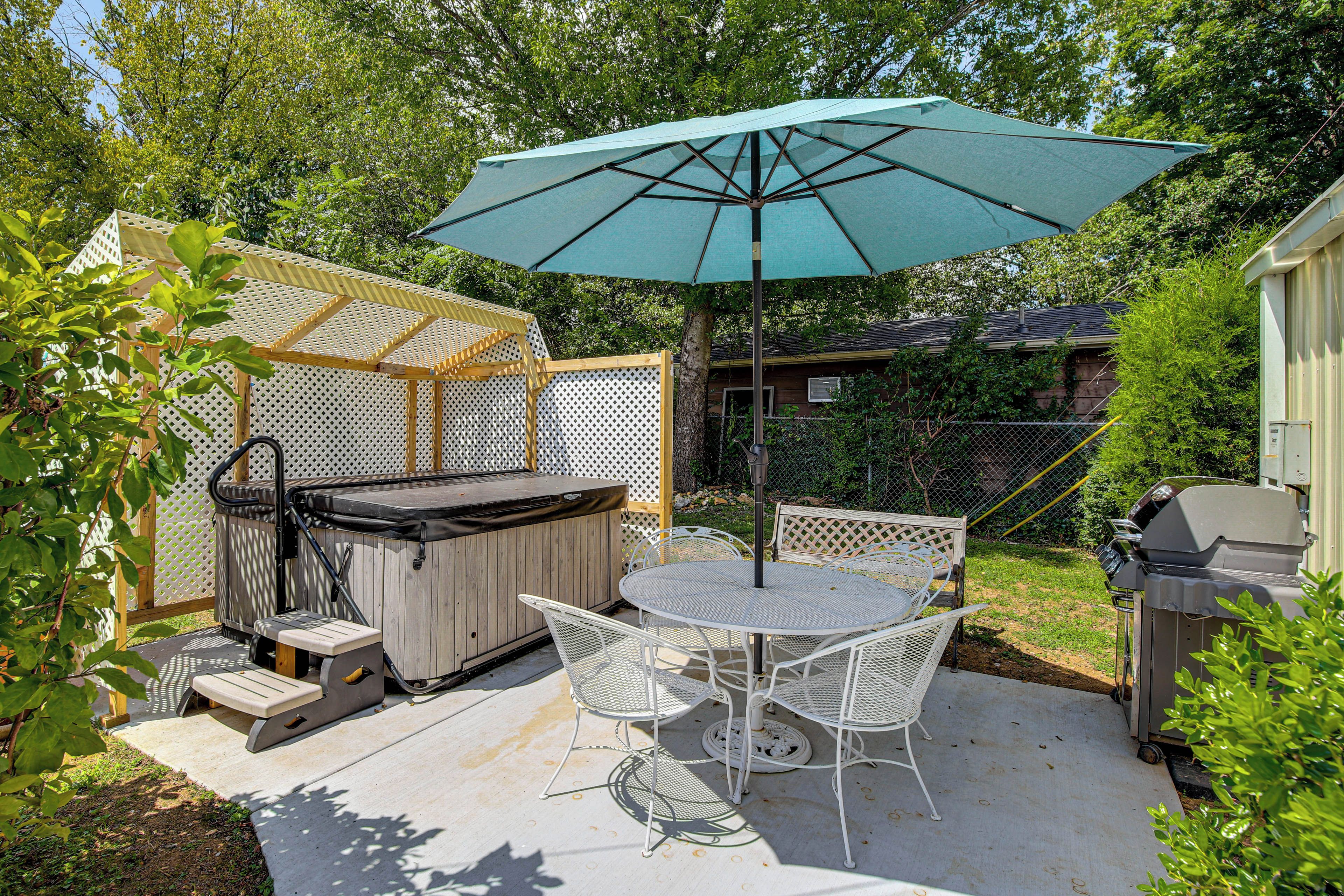 A backyard patio with a hot tub, a table and chairs, and a large umbrella.