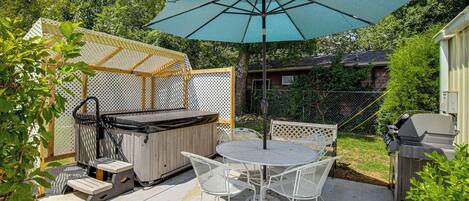 A backyard patio with a hot tub, a table and chairs, and a large umbrella.