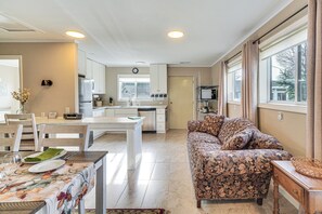 Eine moderne Küche mit weißen Schränken, einem Essplatz mit Tellern und Gläsern sowie ein Couch mit Muster im Wohnbereich.