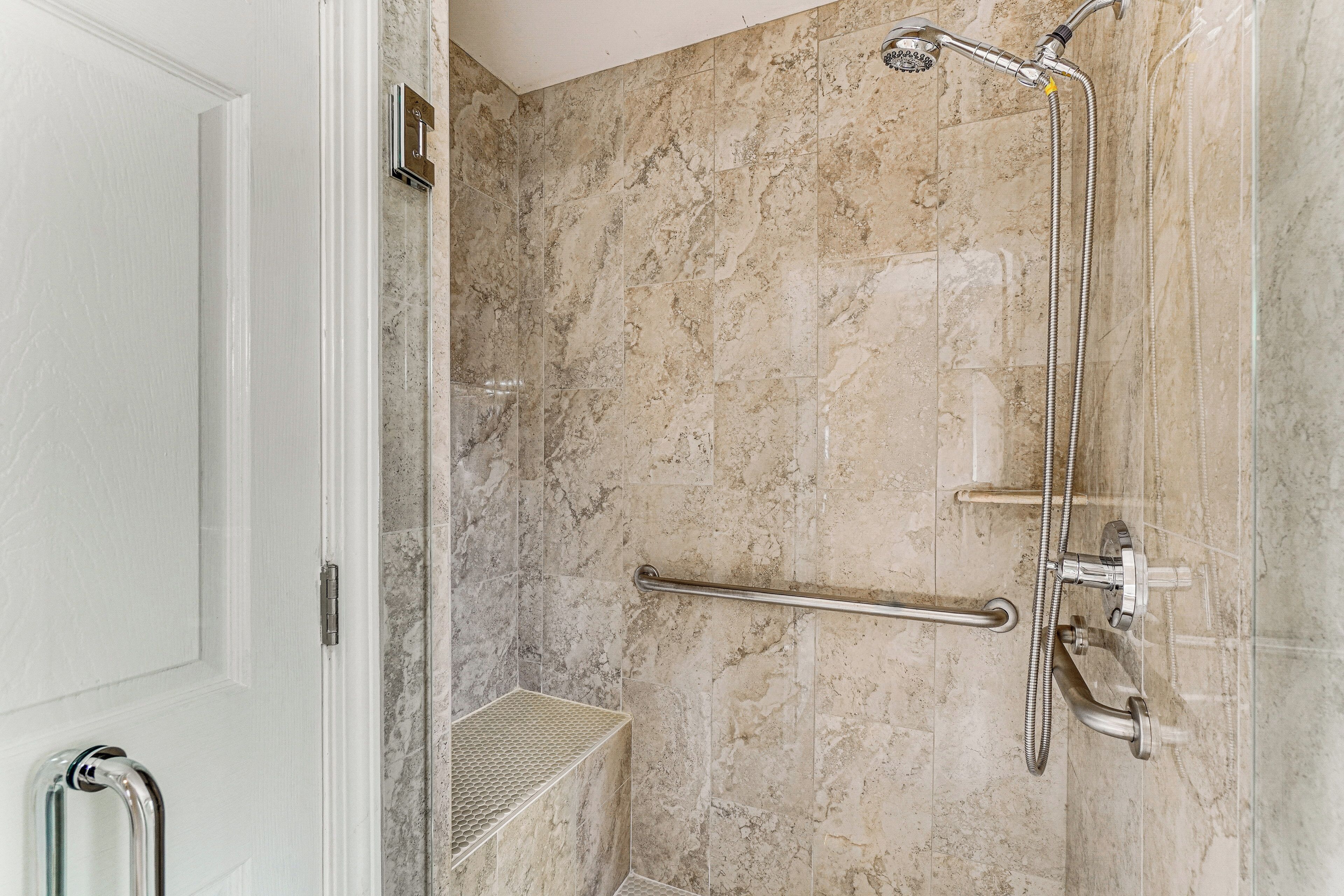 Een badkamer met een douche, marmeren wanden en een handgreep.