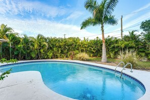 A swimming pool with a curved edge, surrounded by lush greenery and palm trees. - 5 Mi to Downtown St Pete: Private Oasis w/ Yard (St. Petersburg)