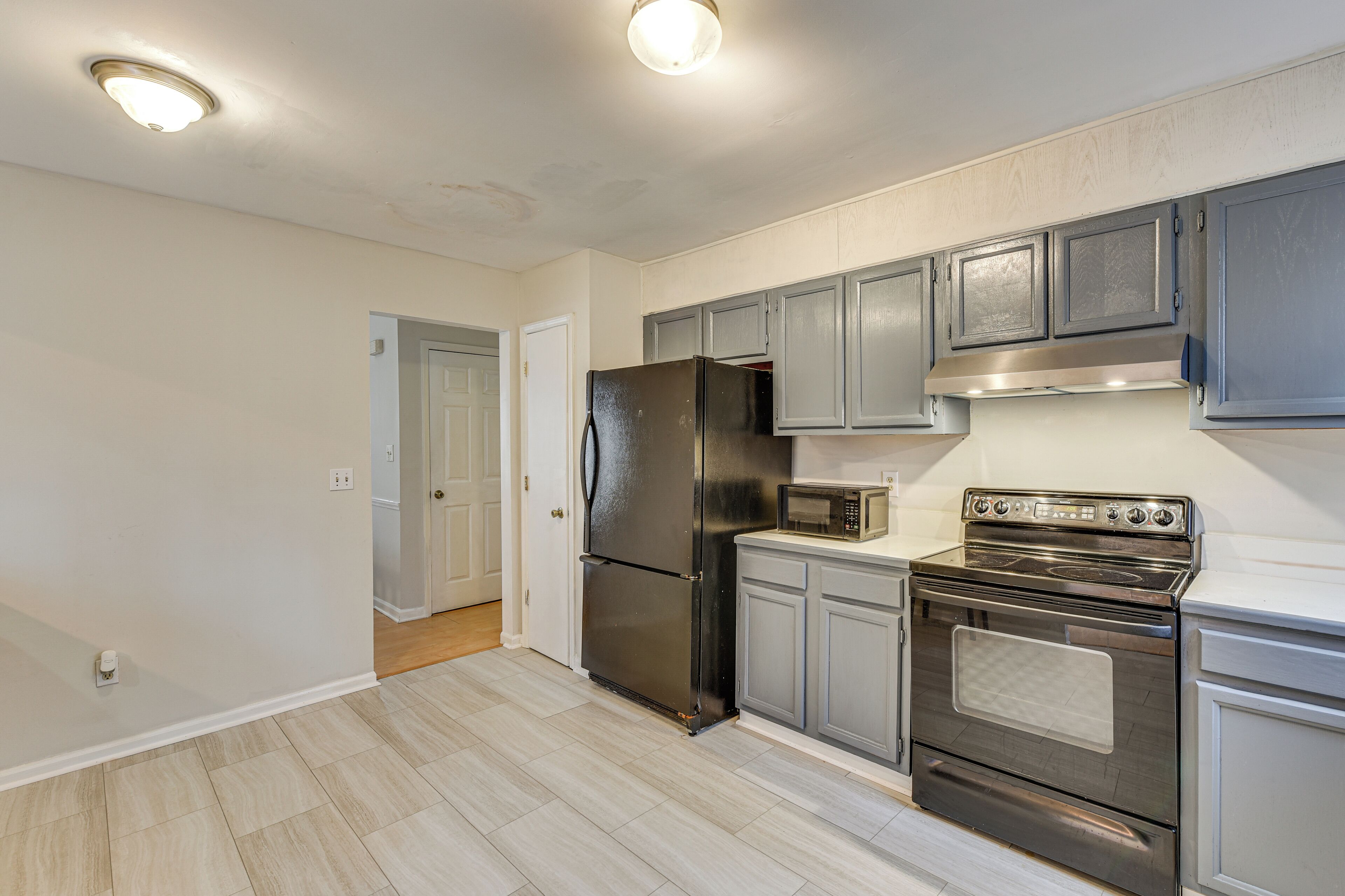 A modern kitchen with grey cabinets, a stainless steel refrigerator, a microwave, and an oven.