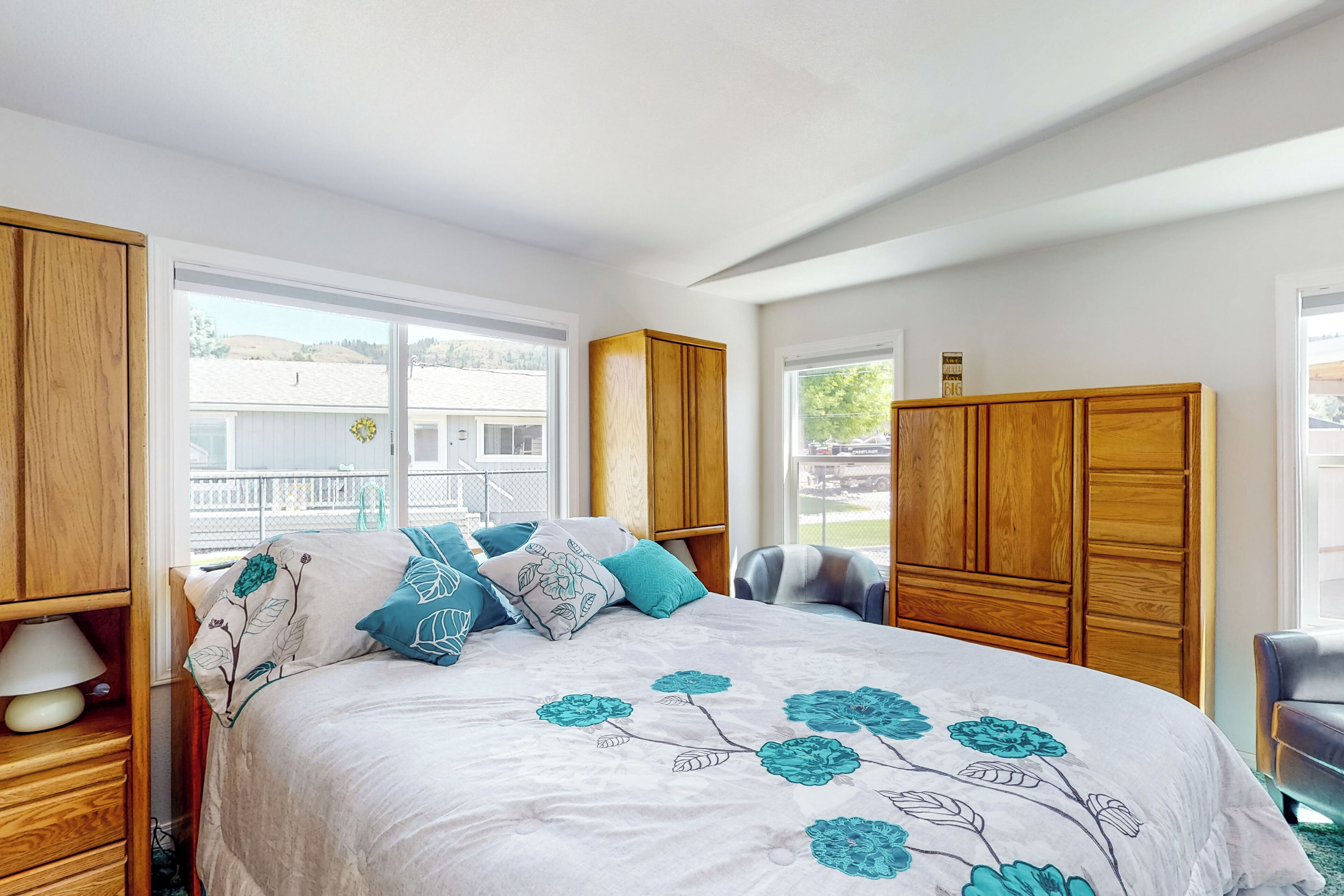 A bedroom with a large bed, wooden wardrobe, and a window with a view of a house and hills.