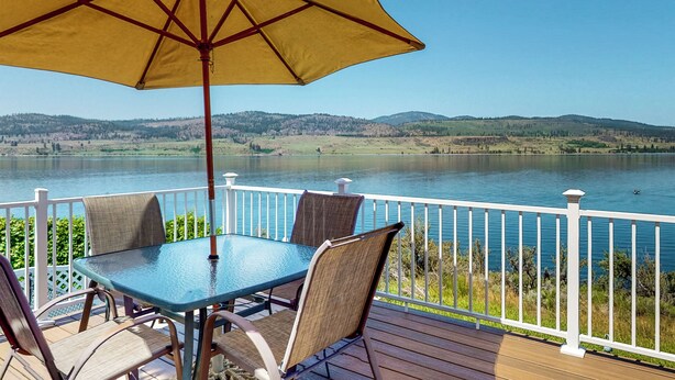 A deck with a table and chairs, a yellow umbrella, and a view of a lake and hills.