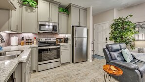 A modern kitchen with stainless steel appliances, a built-in oven, and a microwave. There is a seating area with a leather couch and a small wooden table. - 3 Mi to Downtown Edinburg: Quiet Condo w/ Patio (Edinburg)