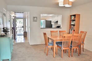 Un coin repas avec une table et des chaises en bois, une bibliothèque et, au fond, une cuisine.