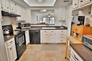 Una cocina moderna con armarios blancos, microondas, estufa, lavavajillas y cafetera.