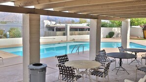 Un patio exterior con piscina, asientos y vista a un edificio al fondo.