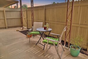 Une terrasse avec une table et des chaises, une balançoire et une clôture en bois.