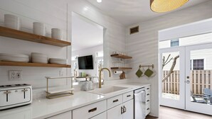 Una cocina moderna con armarios blancos, estantes de madera y un ventanal grande.