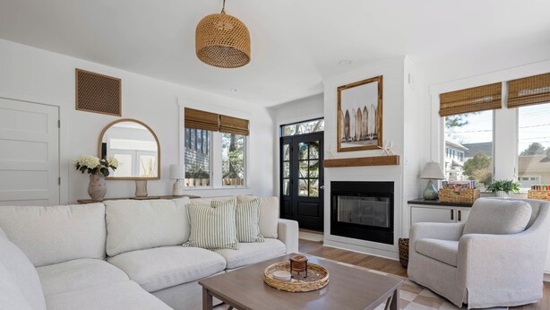 Una sala de estar con sofá, sillón, mesa de centro, chimenea y ventanas grandes con persianas.