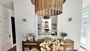 Una cocina moderna con comedor, que incluye una mesa de madera grande, un jarrón de flores y una lámpara colgante de mimbre.