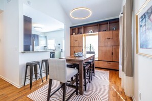 A modern kitchen with wooden cabinets, a dining area with a wooden table and bar stools, and a large mirror on the wall. - Walk to BeltLine | 3 Miles to World Cup Stadium (Atlanta)