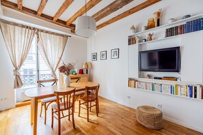 Uma sala de estar acolhedora com uma mesa de jantar de madeira, cadeiras, uma televisão e uma estante de livros.