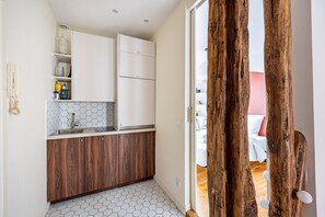 Uma cozinha compacta com armários brancos, painel de azulejos hexagonais e bancada de madeira.