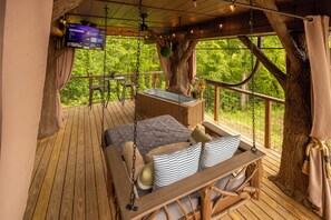 A wooden deck with a bed, a TV, and a view of greenery. - Couples Treehouse Retreat | Outdoor Tub + Starlight Ceiling | Sleeps 4 (Sevierville)