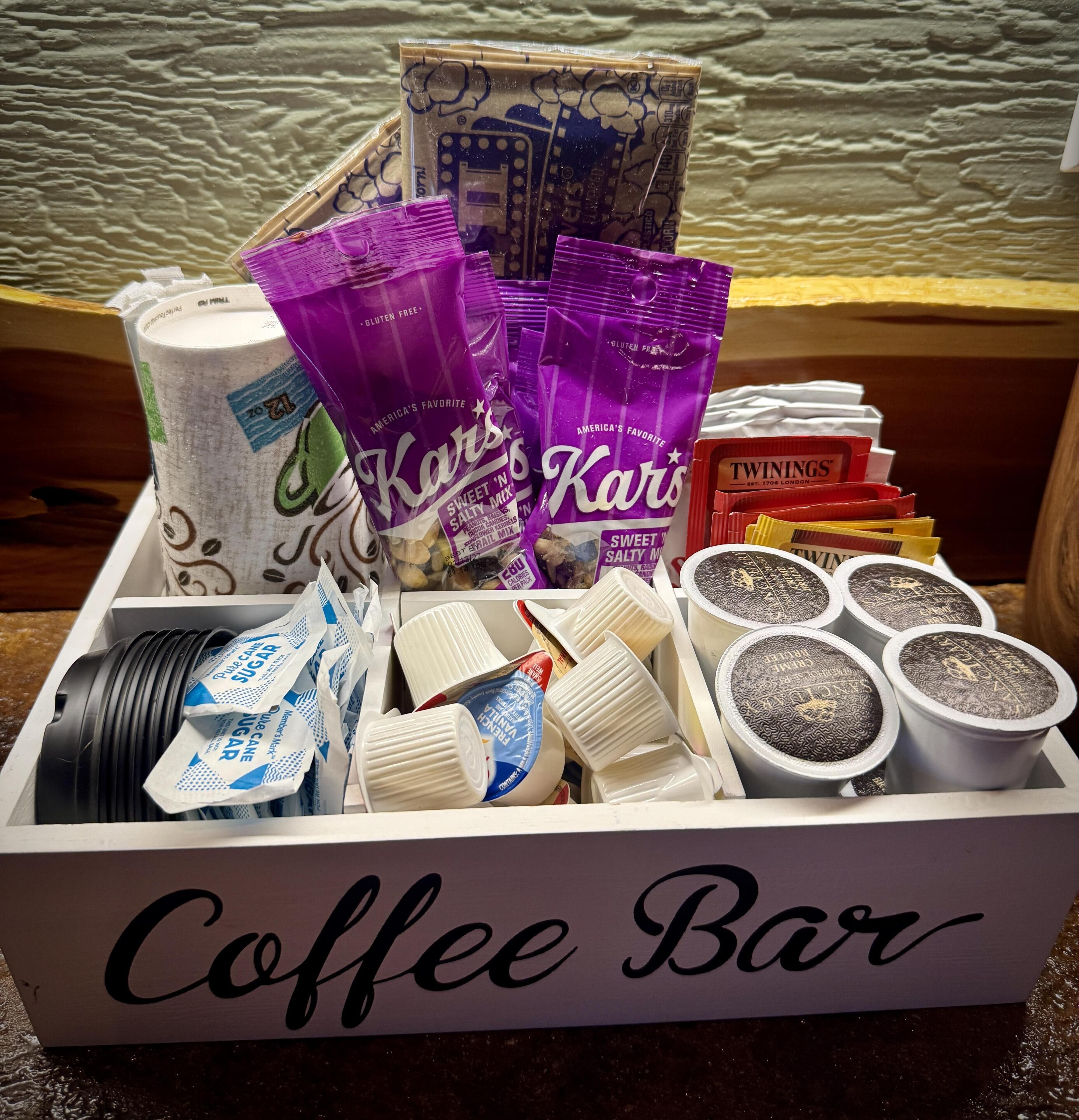A box labeled 'Coffee Bar' containing various coffee-related items like Twinings tea bags, Kars sweet n salty mix, and sugar packets.