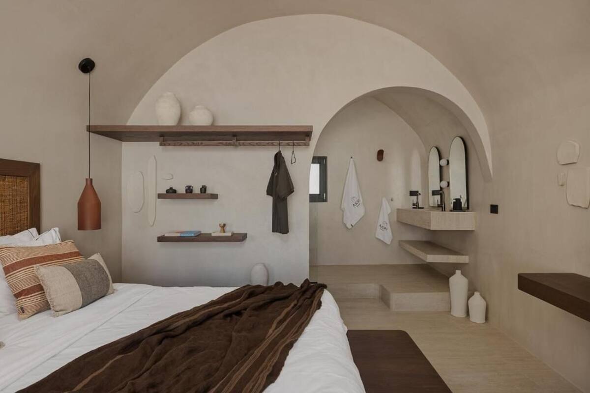 A bedroom with a bed, a hanging light, shelves with toiletries, and a bathroom with a mirror and towel rack.