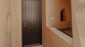 Un corridoio stretto con una porta scura, una piccola nicchia con uno scaffale e una scala che conduce a un piano superiore.