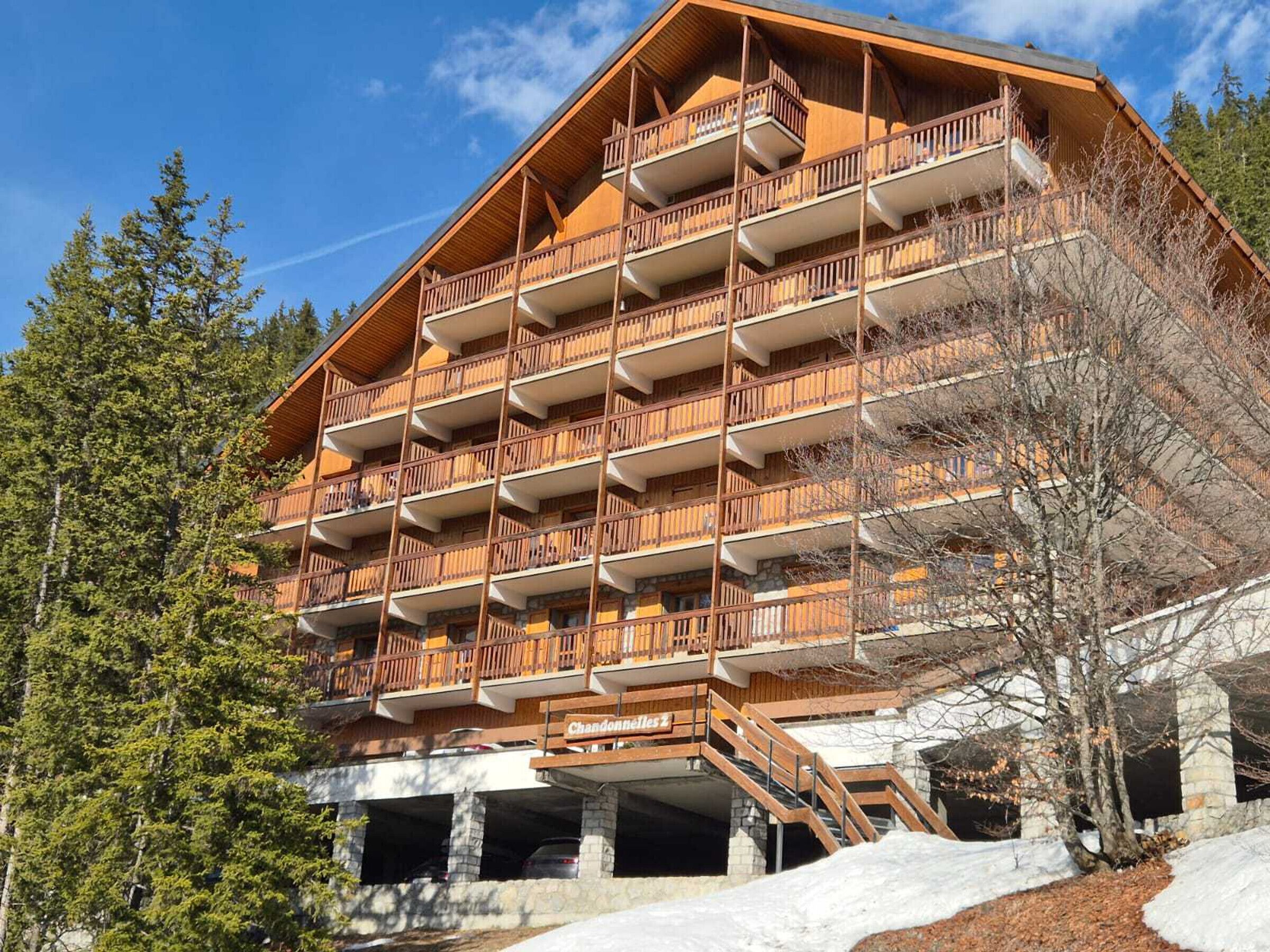 A multi-story wooden building with balconies, a sign reading 'Chandonelles 1', and a stone base.