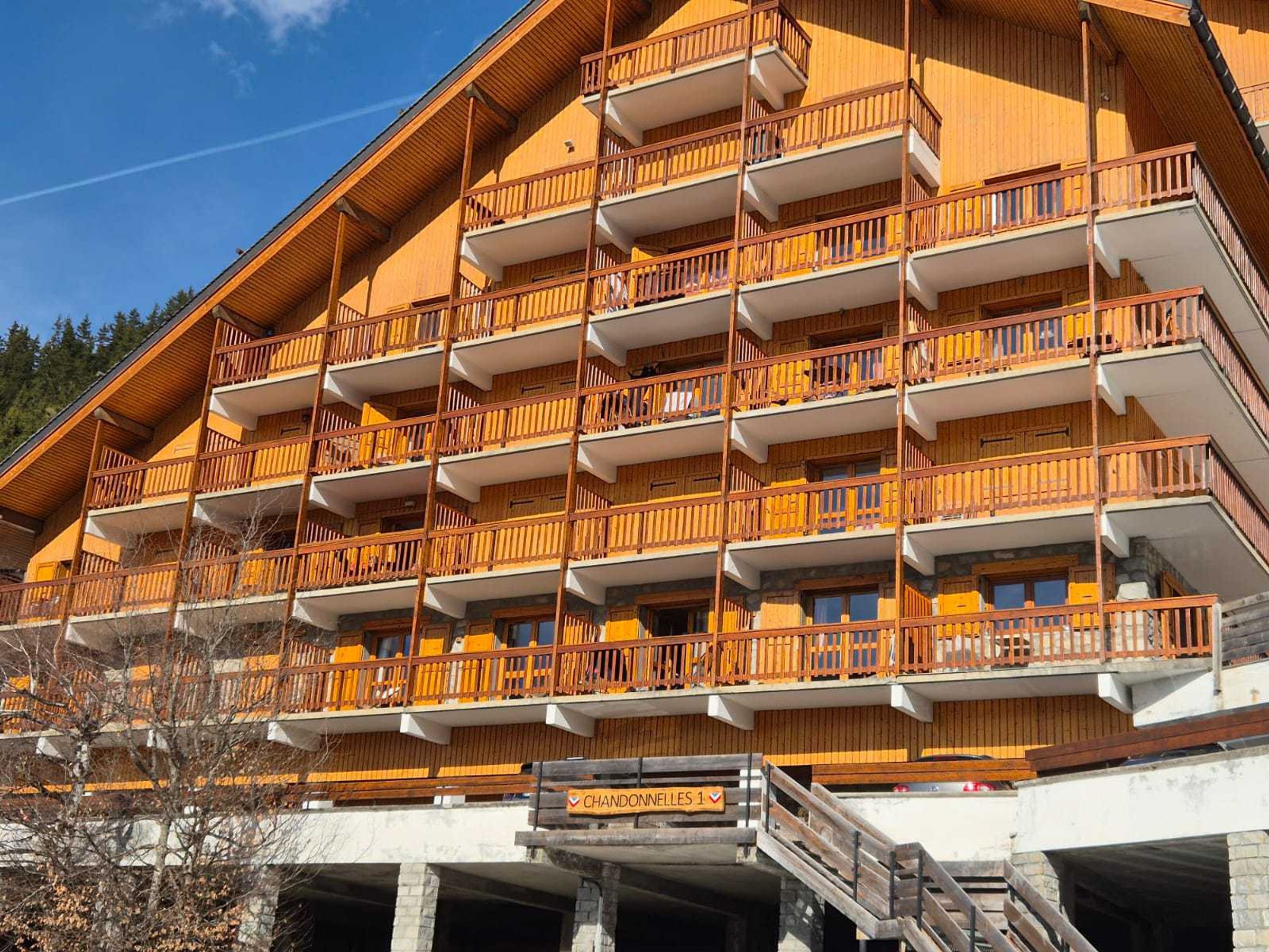 A multi-story hotel with balconies, a sign indicating 'CHANDONNELLES 1', and a ski lift visible in the background.
