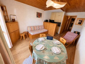 A compact room with a dining table set for four, a sofa, a kitchenette, and a small bed. - Apartment near slopes with balcony, valley view (Méribel)