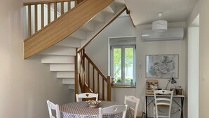 A dining area with a wooden staircase, white chairs, and a table with a patterned tablecloth.