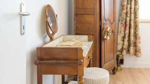 A wooden dresser with a mirror, a small table with a tray, and a floral curtain.