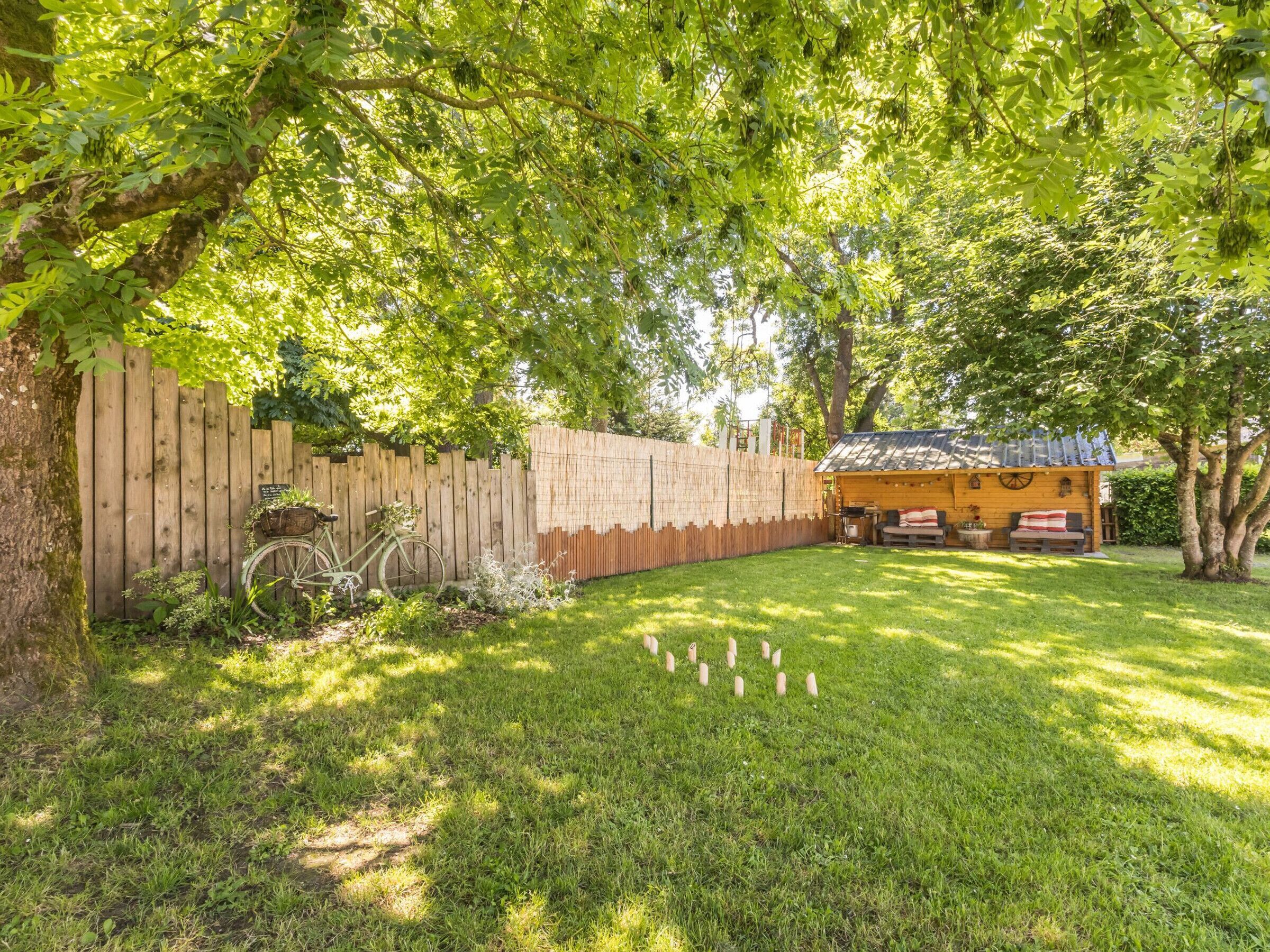 A backyard with a wooden fence, a bicycle, a small wooden structure, and a grassy lawn.