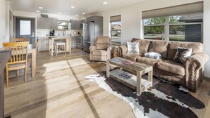 A spacious living area with a wooden dining table, a sofa, and a kitchen in the background.
