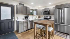 A modern kitchen with stainless steel appliances, wooden bar stools, and a large refrigerator.