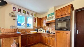 A kitchen with wooden cabinets, a tiled floor, a stove, and a microwave. - 3-room house in Carnac - 4 ppl, terrace and garden (Carnac)