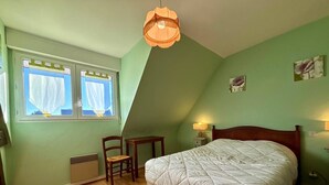 A bedroom with a bed, a chair, a small table, a window with curtains, a hanging light fixture, and a wall-mounted lamp. - 3-room house in Carnac - 4 ppl, terrace and garden (Carnac)