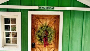 Un bâtiment vert avec une porte en bois portant l’inscription « TOILETTES » et une petite fenêtre sur la gauche.