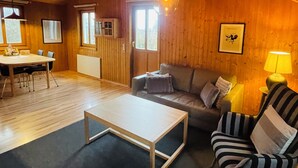 Interior acogedor de una cabaña de madera con comedor, un sofá, un sillón a rayas y una lámpara.