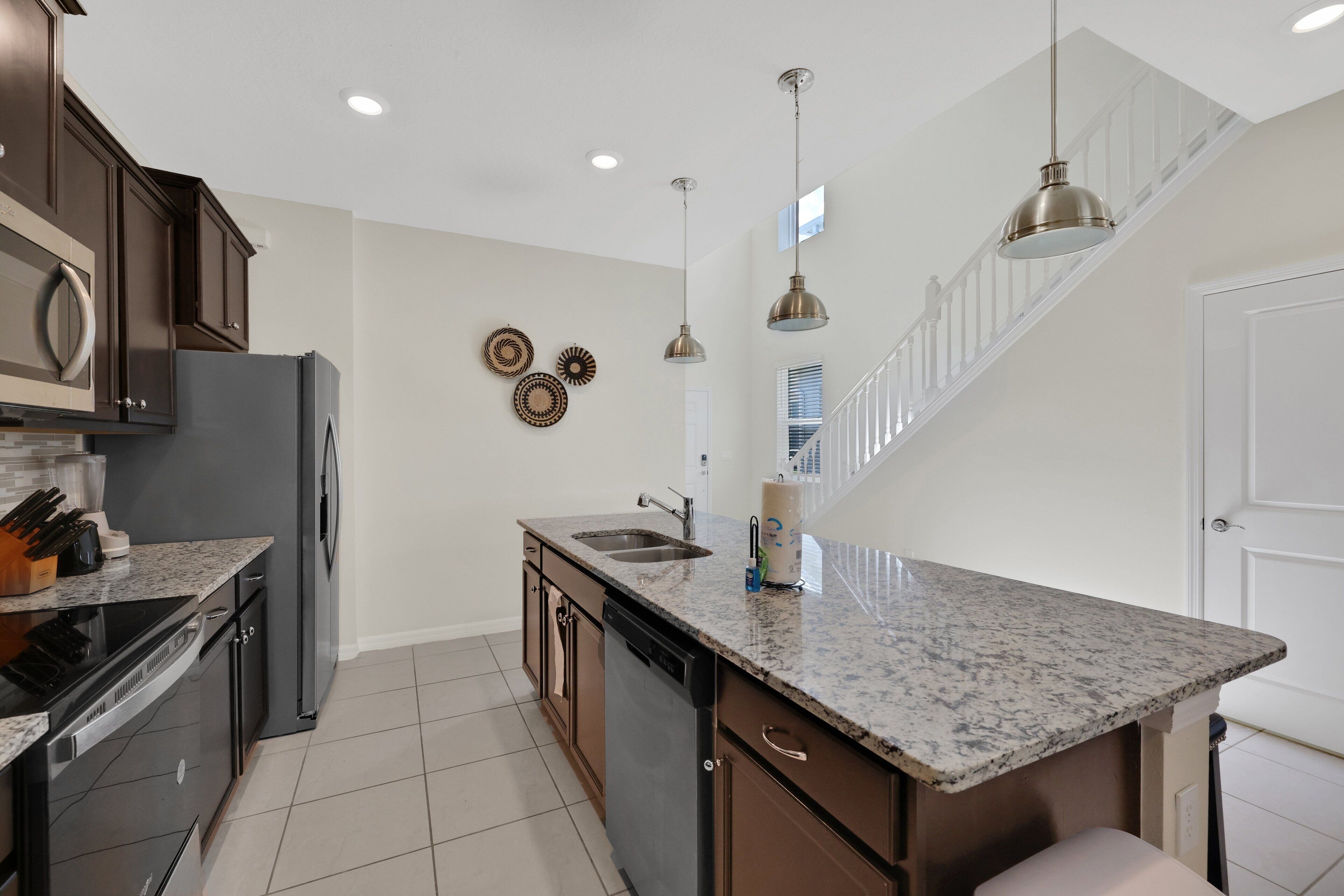 A kitchen with granite countertops, stainless steel appliances, and pendant lighting.